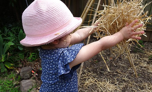 Photo of a child using hay to develop knowledge and skills of every day experiences.